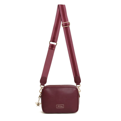 A berry red faux leather cross body bag with adjustable patterned canvas strap