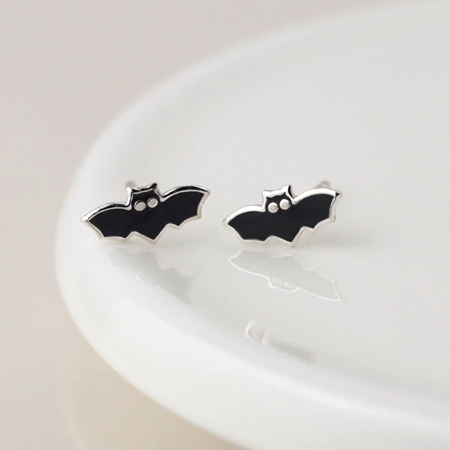 Pair of silver stud earrings shaped like bats with enamelled details