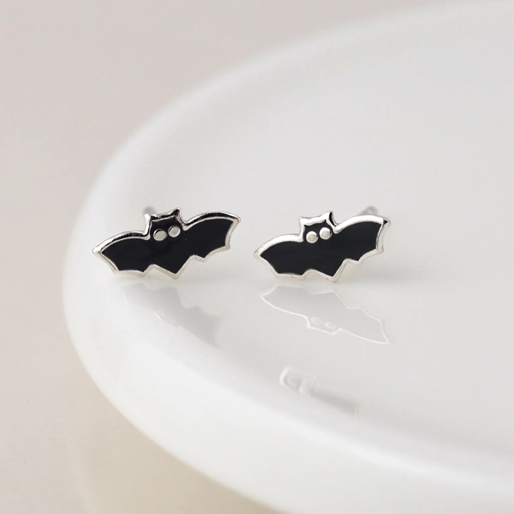 Pair of silver stud earrings shaped like bats with enamelled details