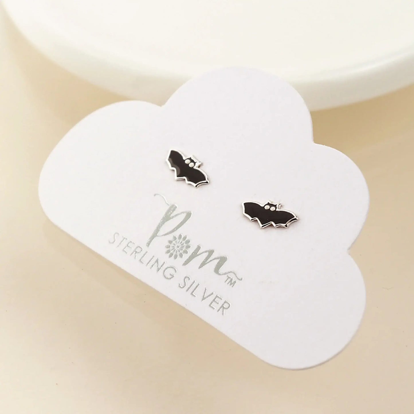 Pair of silver stud earrings shaped like bats with enamelled details on card