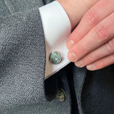 Model wearing round silver cufflinks with stag's head design in moss green enamel 