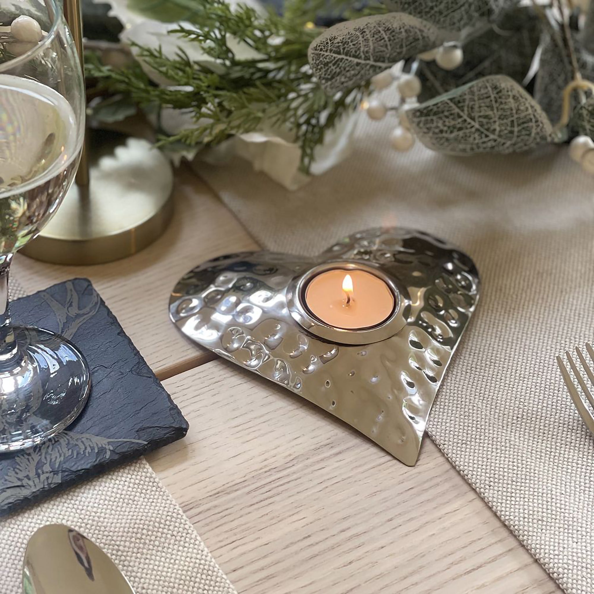 A hammered texture polished steel heart tealight holder staged on a table