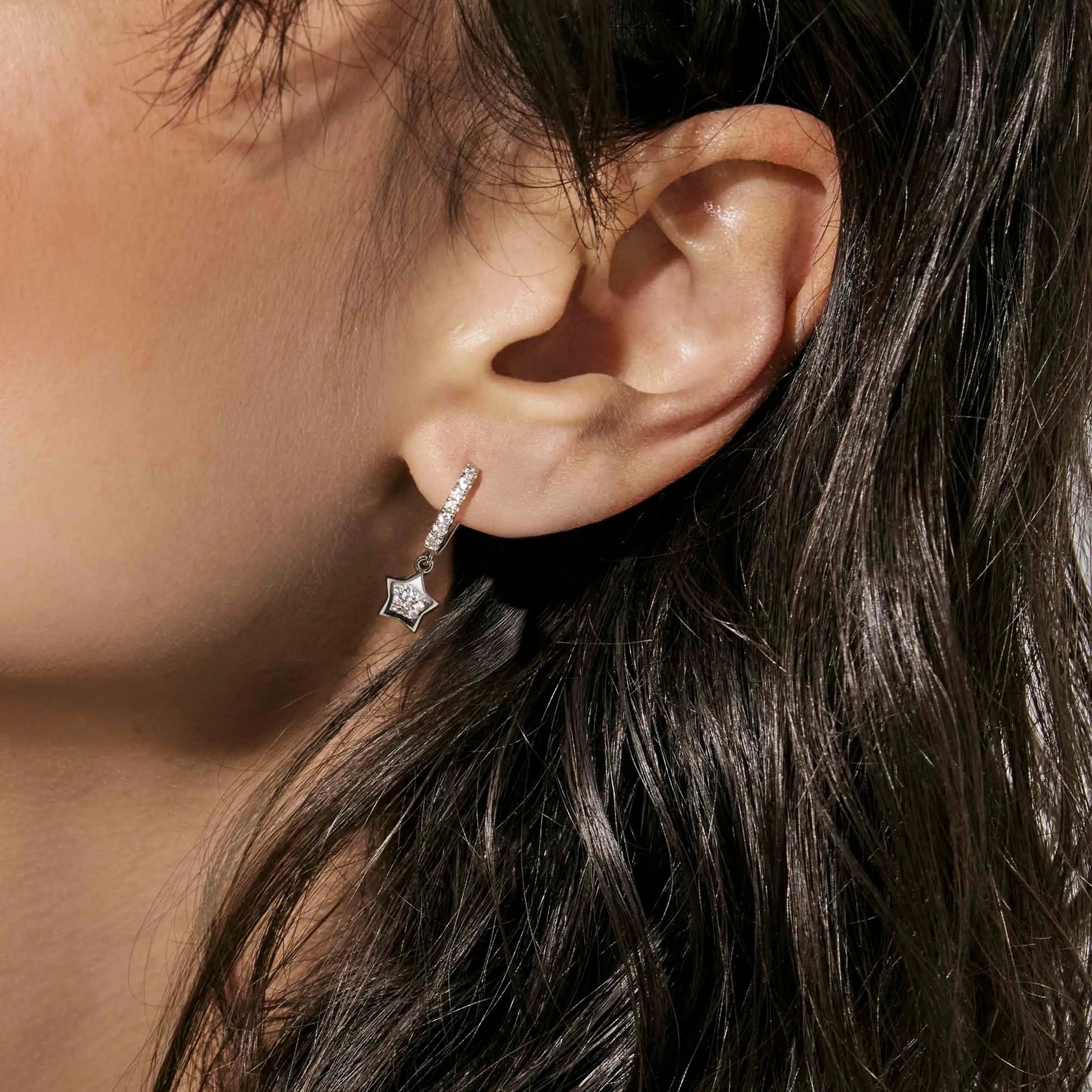 Model wearing silver hoop earrings featuring star shaped drops with smaller pave CZ star cluster inside
