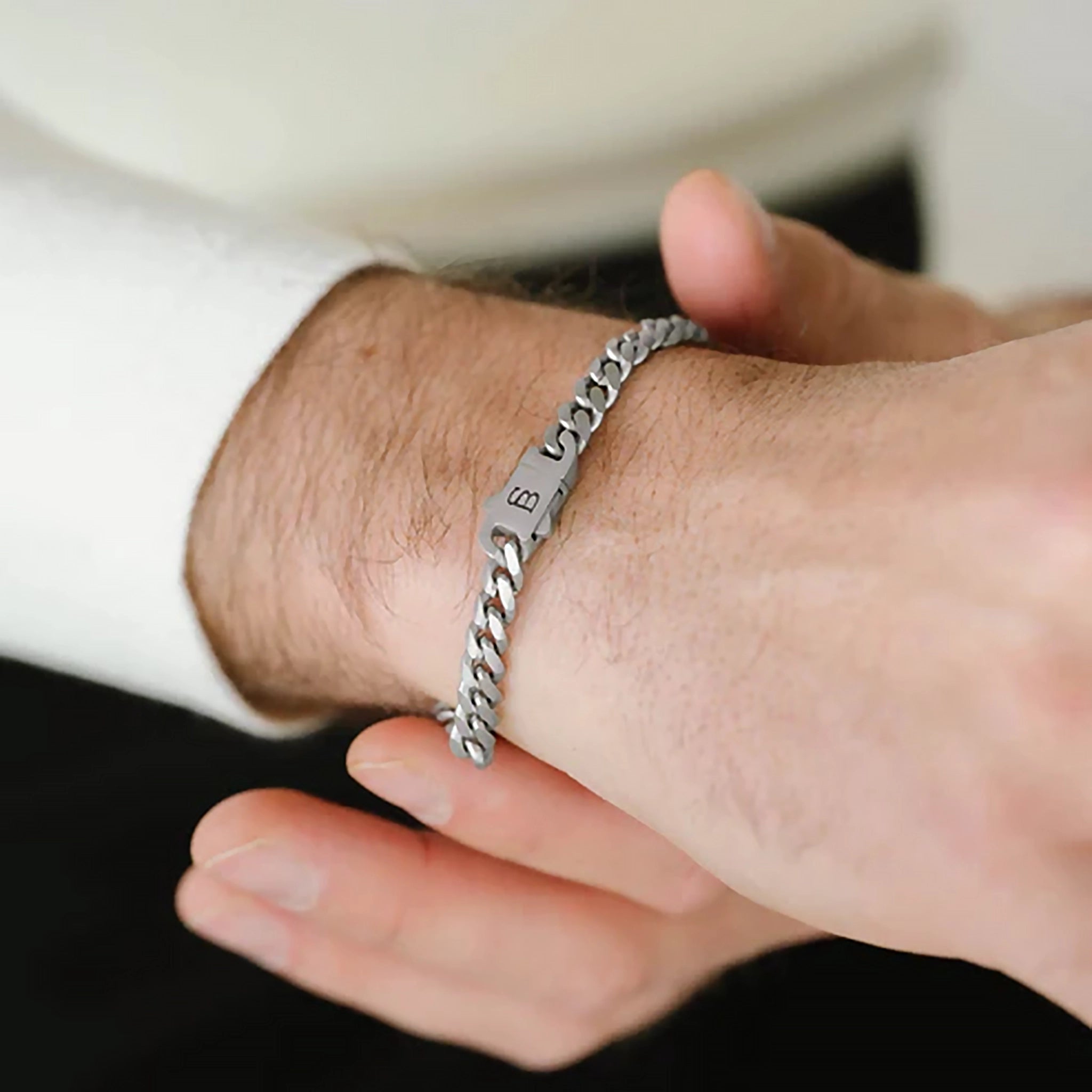 Model wearing a silver stainless steel chain bracelet with monogramed clasp