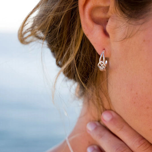 Model wearing a pair of small hoop earrings with Celtic knot figure 8 shape