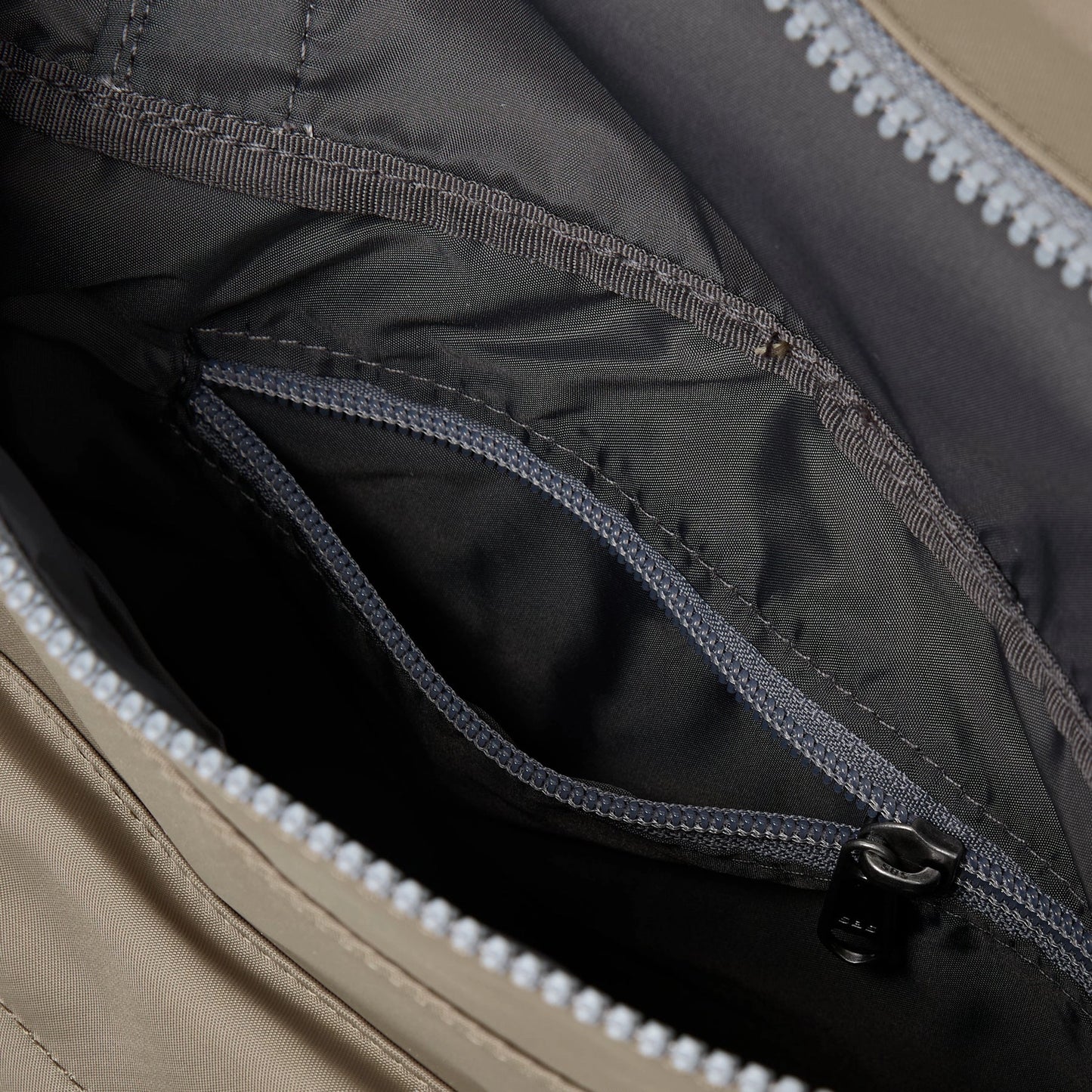 A square taupe nylon bag with grey cotton strap and roll top with internal zip pocket