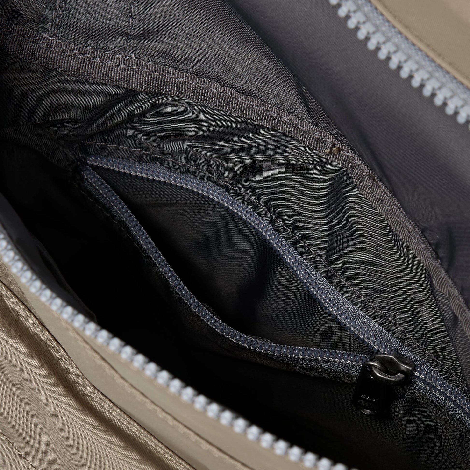 A square taupe nylon bag with grey cotton strap and roll top with internal zip pocket