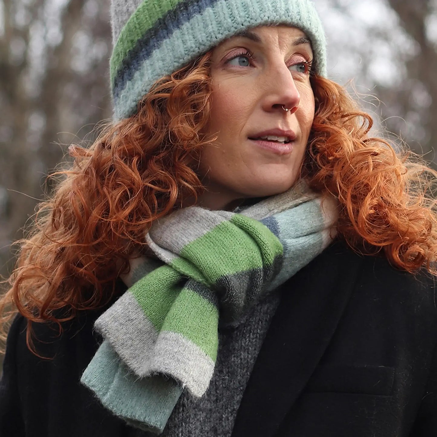 Model wearing a striped colour block knitted scarf in grey, blue and green