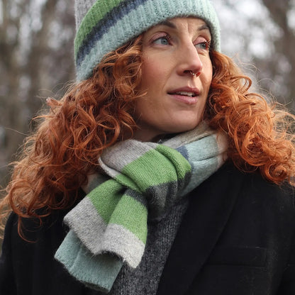 Model wearing a striped colour block knitted scarf in grey, blue and green