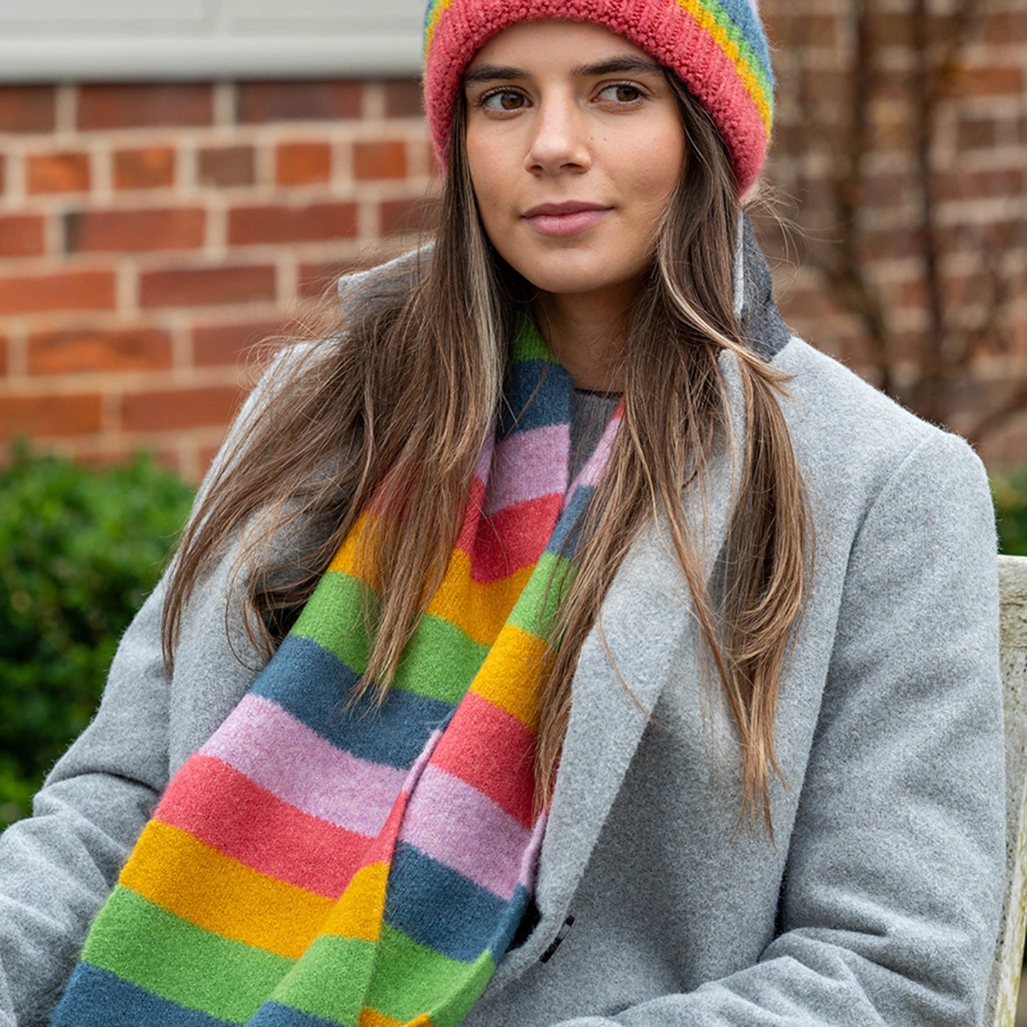 Model wearing knitted scarf with rainbow colour block stripes