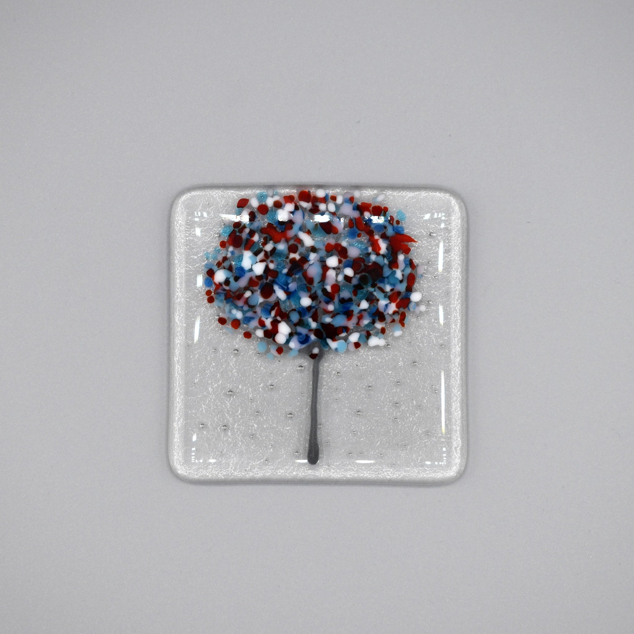 A clear glass square coaster with a blue & red tree design