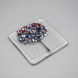 A clear glass square coaster with a blue & red tree design - side