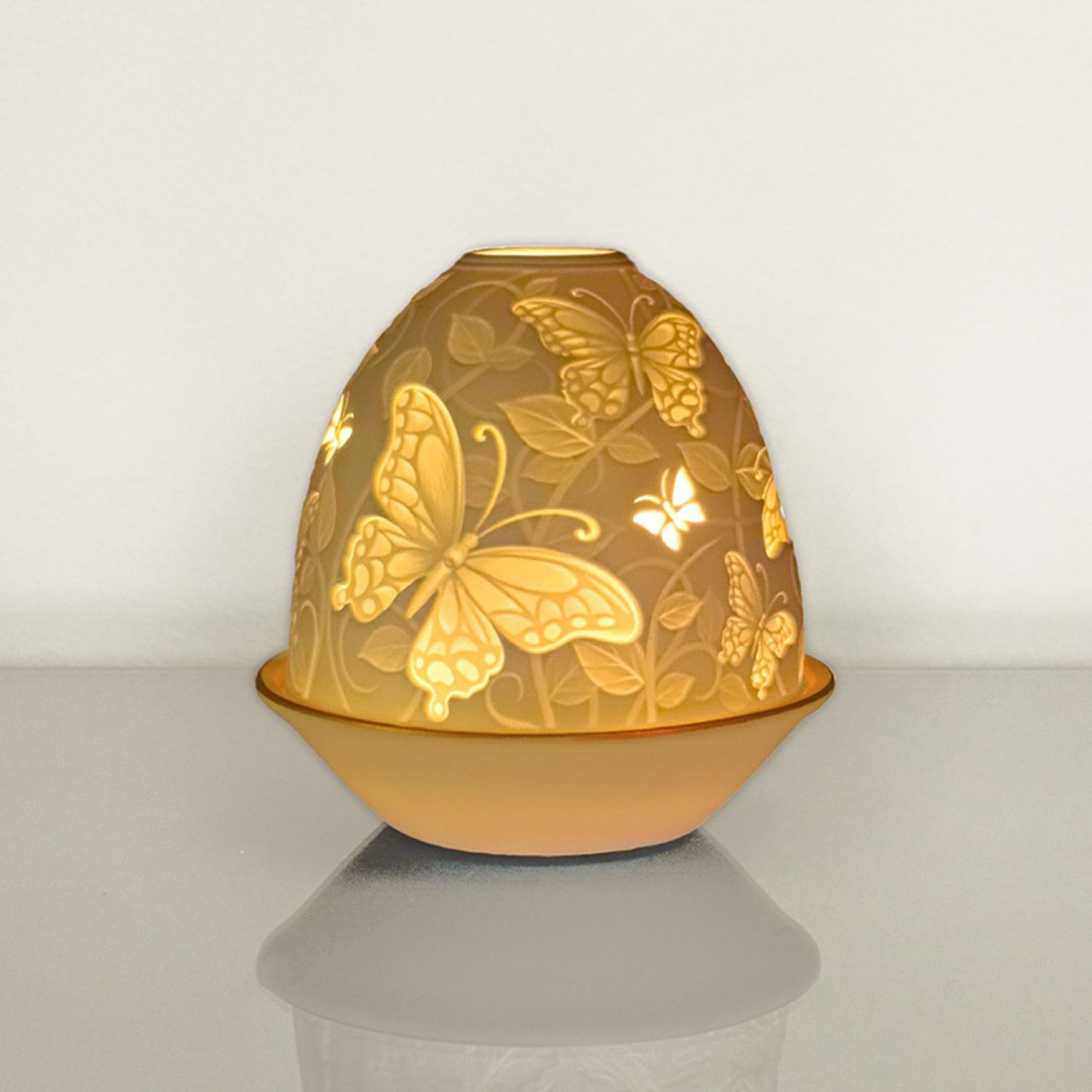 White porcelain tall dome candle holder with engraved butterflies and gold rimmed plate lit up