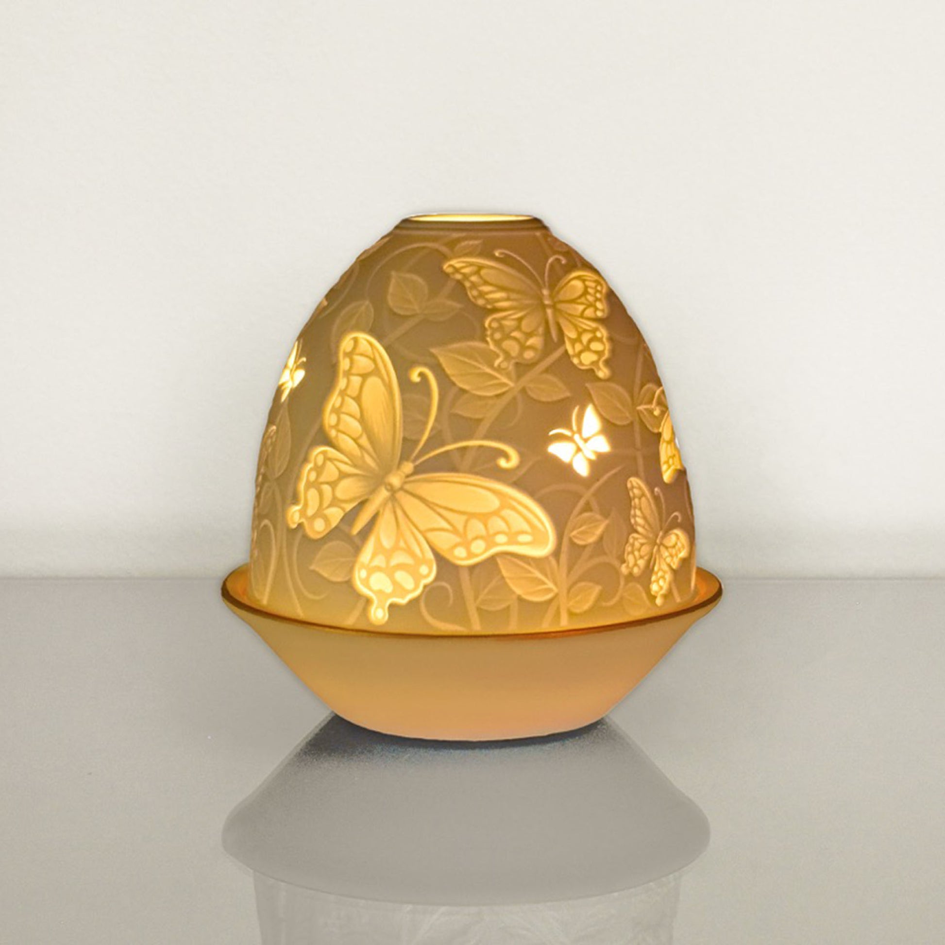 White porcelain tall dome candle holder with engraved butterflies and gold rimmed plate lit up