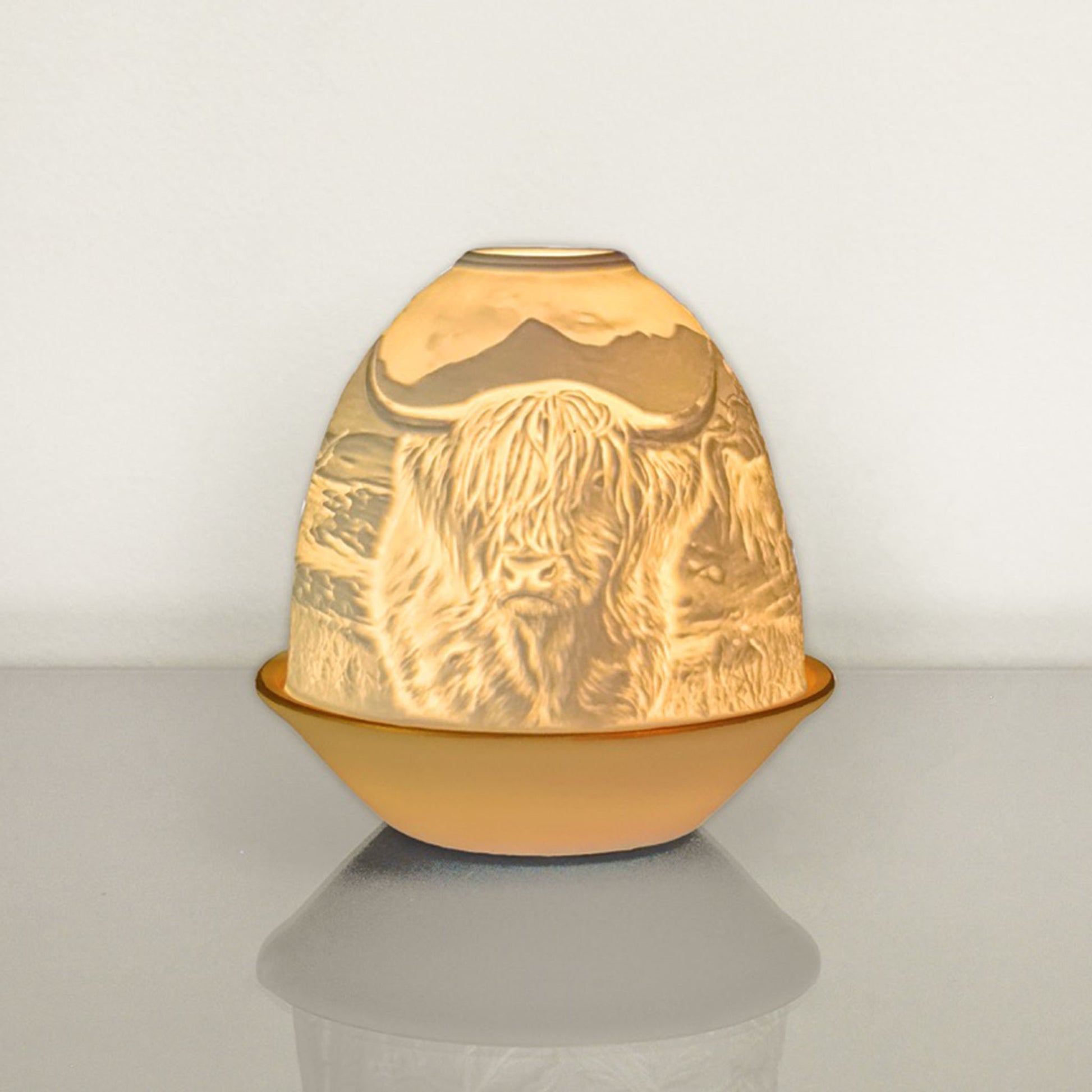 White porcelain tall dome candle holder with engraved Highland cow and gold rimmed plate lit up