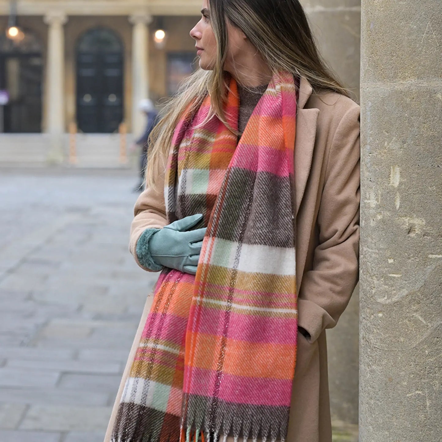 Model wearing a tartan check scarf in orange, pink and brown with tassel fringe