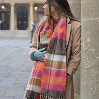 Model wearing a tartan check scarf in orange, pink and brown with tassel fringe