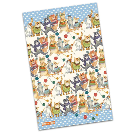 A tea towel featuring a repeat illustration of cats in winter clothes and knitting