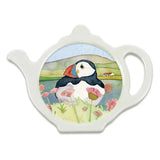 A teabag tiday in the shape of a teapot, featuring an illustration of a little puffin on a water colour landscape