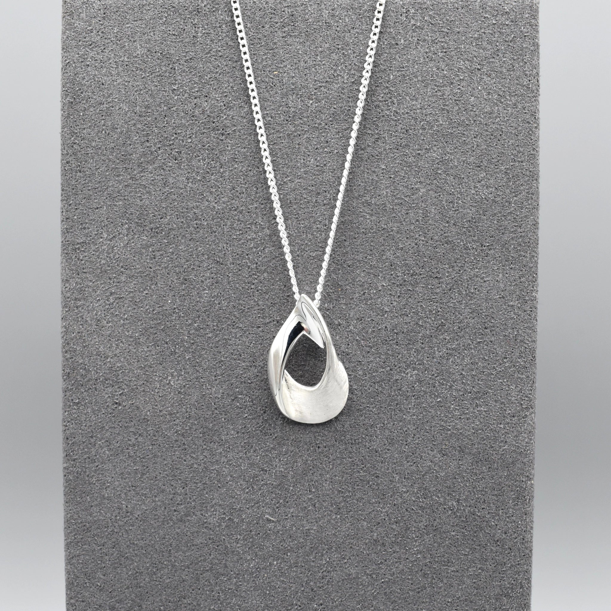 A silver pendant shaped like an open twisted teardrop with a matt and shiny finish