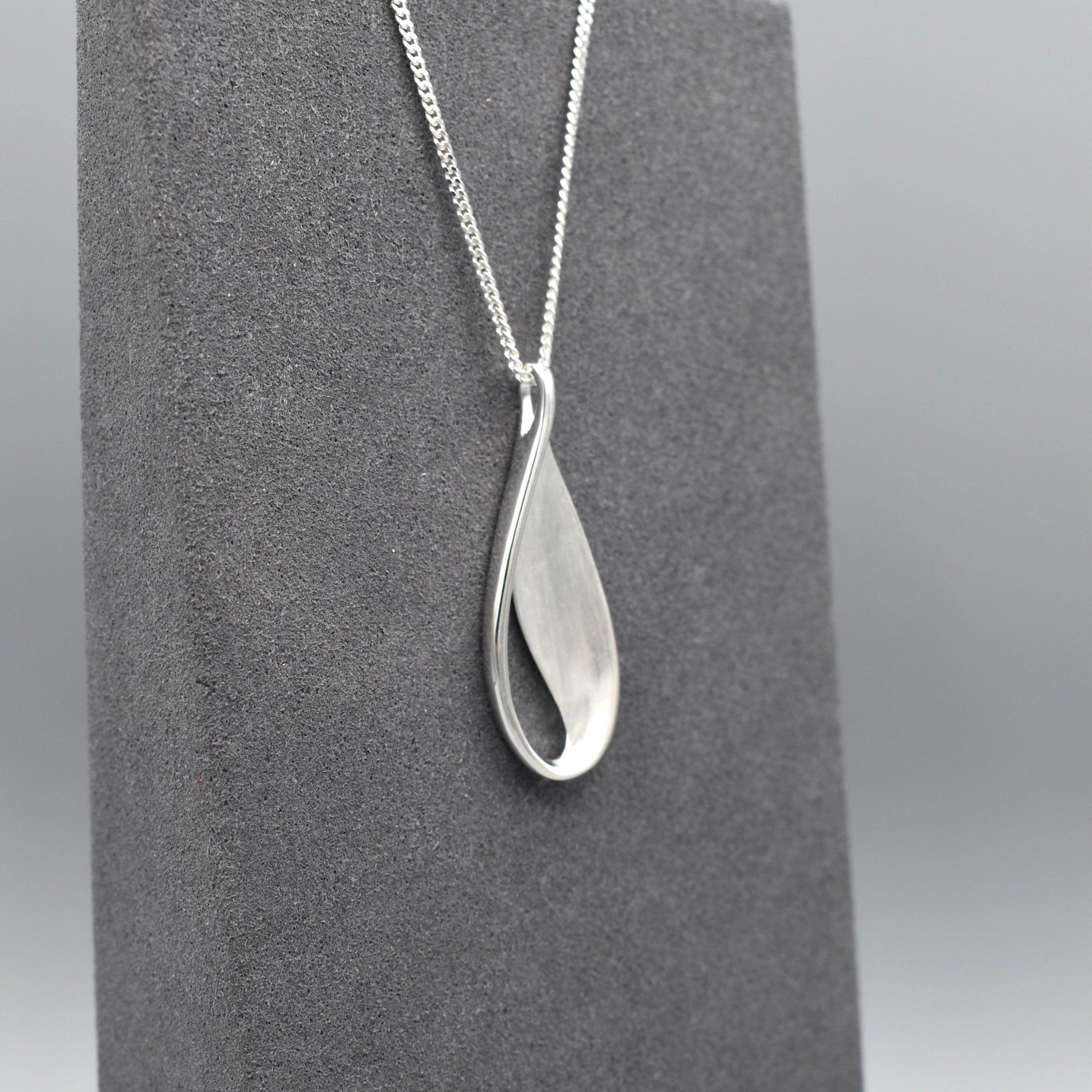 A silver teardrop leaf shaped pendant with matt texture