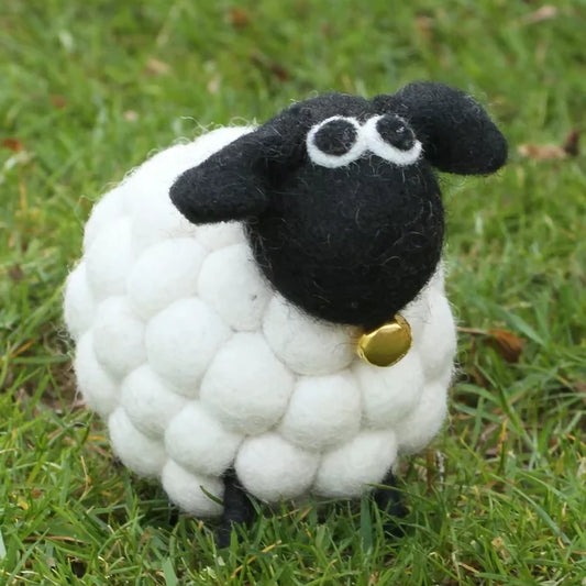 A white pompom sheep figurine with a brass bell in the grass
