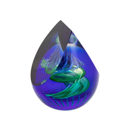 A chisel shaped glass paperweight with swirling purple and blue, a thistle head in the centre, and bubble details side
