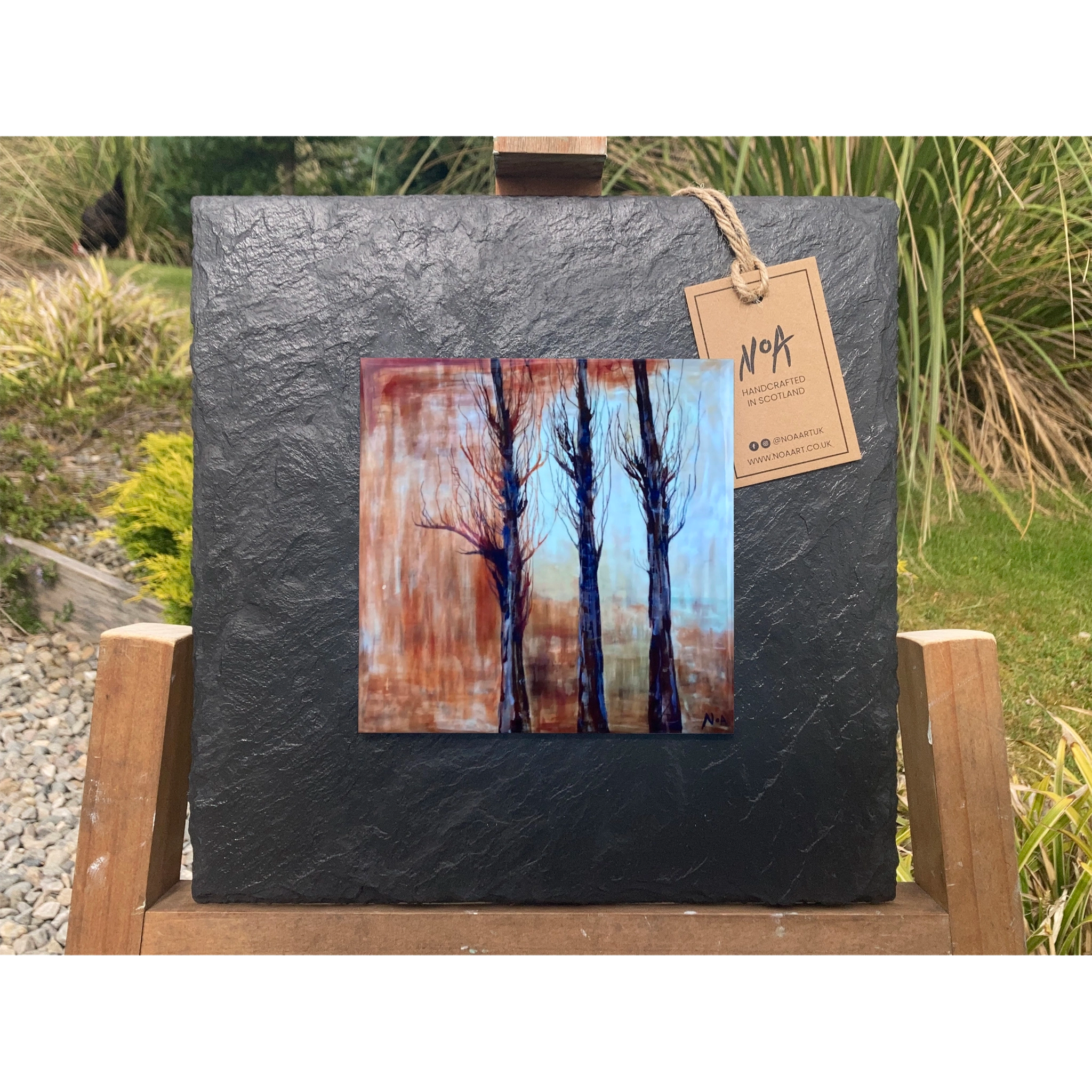 A tile mounted on slate featuring a textured painting of bare trees and autumn colours