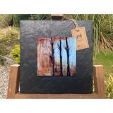 A tile mounted on slate featuring a textured painting of bare trees and autumn colours