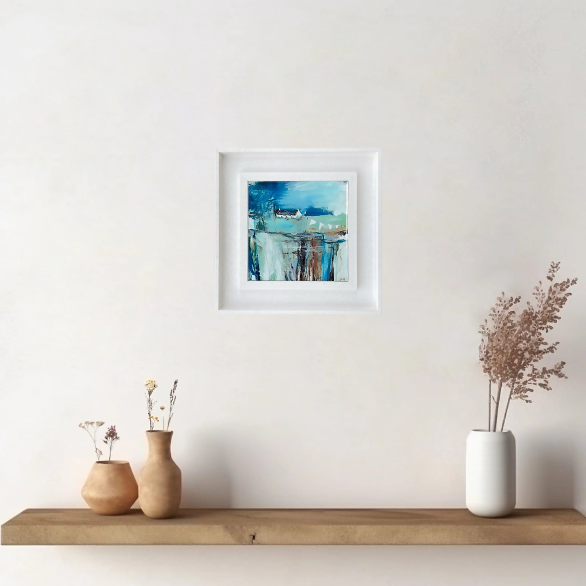 White framed art tile featuring a small white bothy in a vibrant blue setting hanging