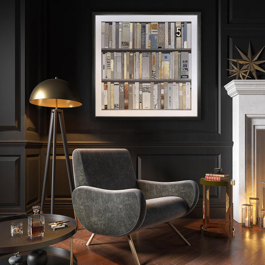 Framed print of mixed media books with raised paper details and metallic paper in vintage style hanging in dark room.