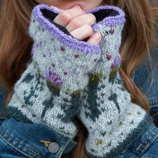 Model wearing a pair of knitted handwarmers in grey with a repeating thistle pattern and hearts