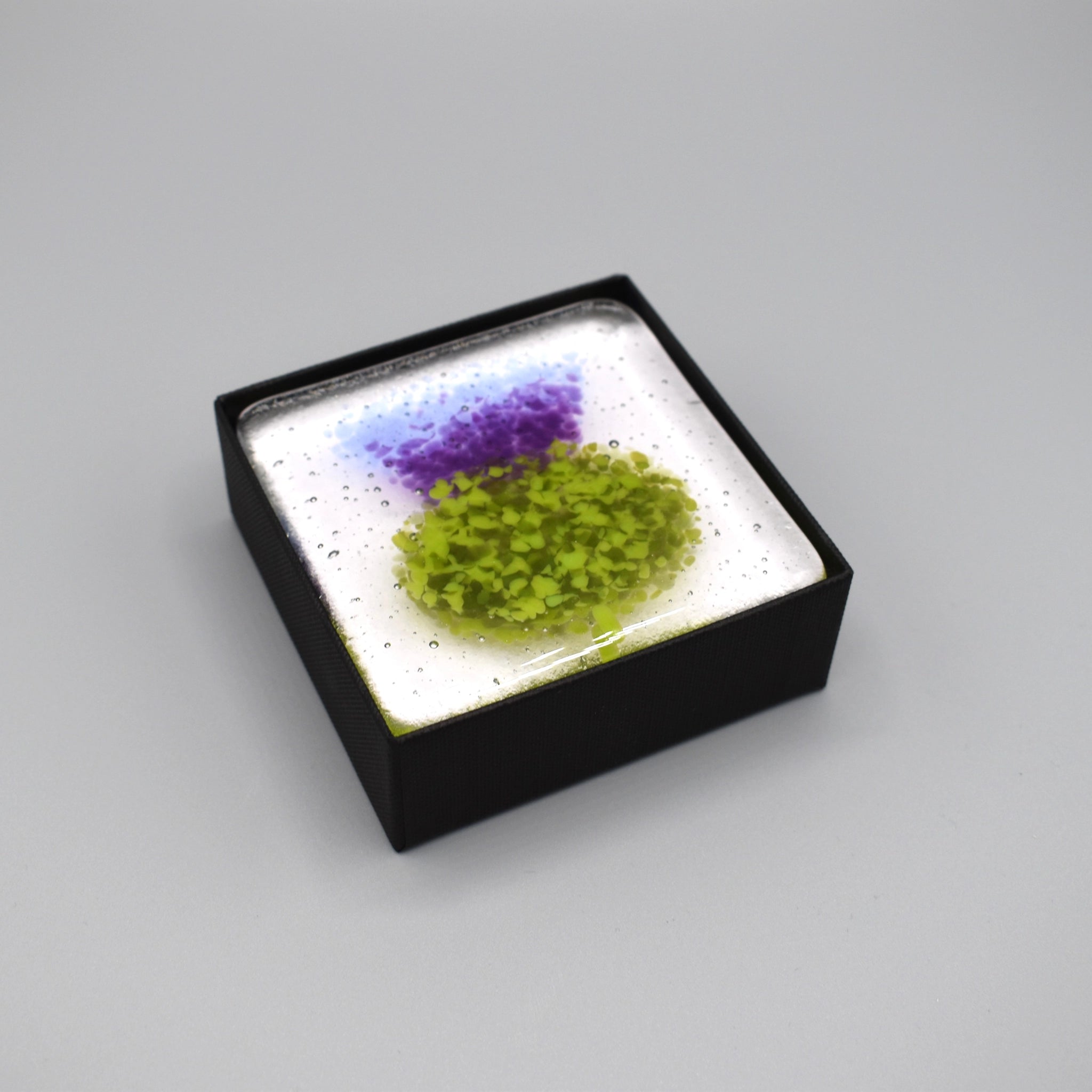 A clear glass square coaster with a purple thistle design in black box