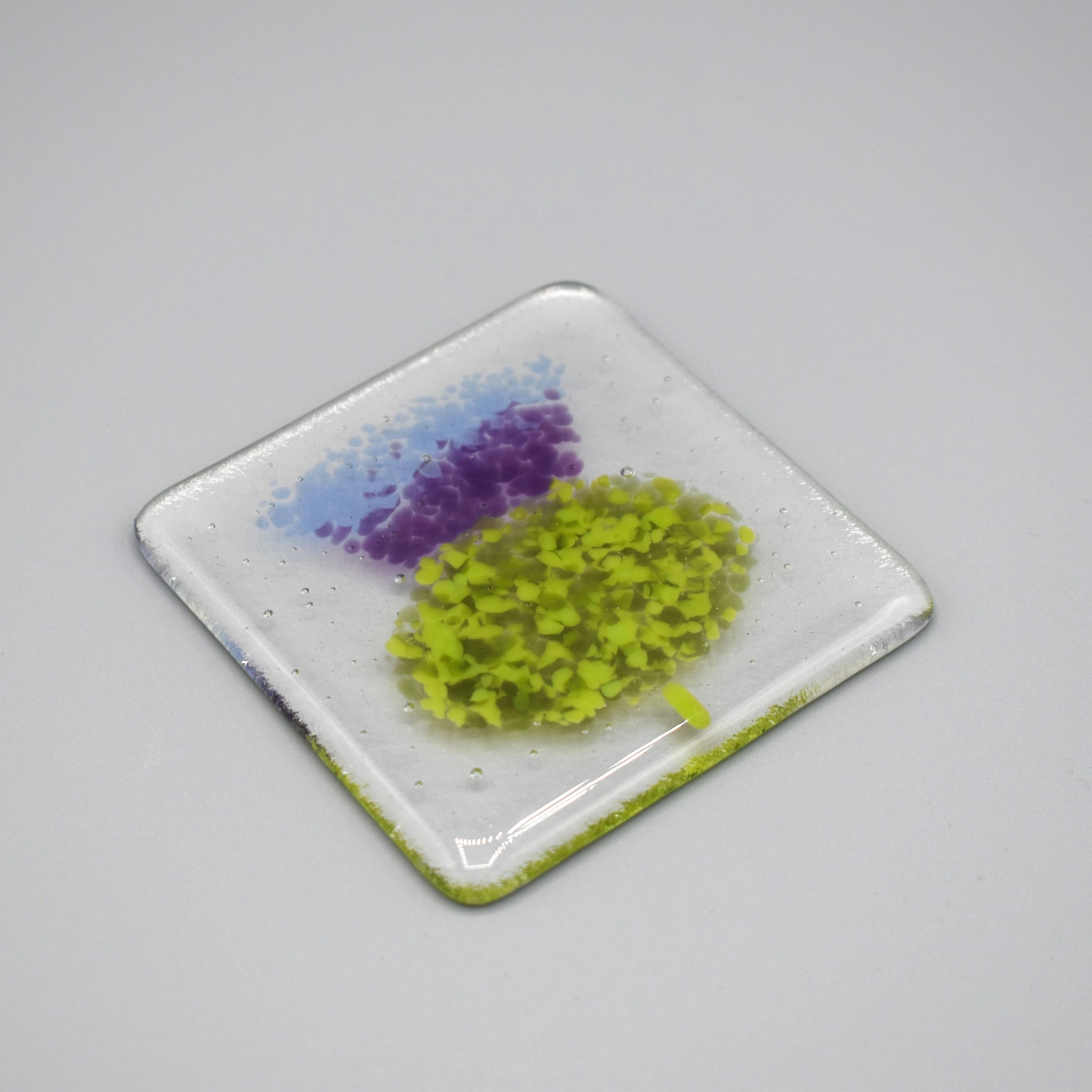 A clear glass square coaster with a purple thistle design