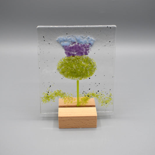 A square glass ornament featuring a thistle and a wooden stand