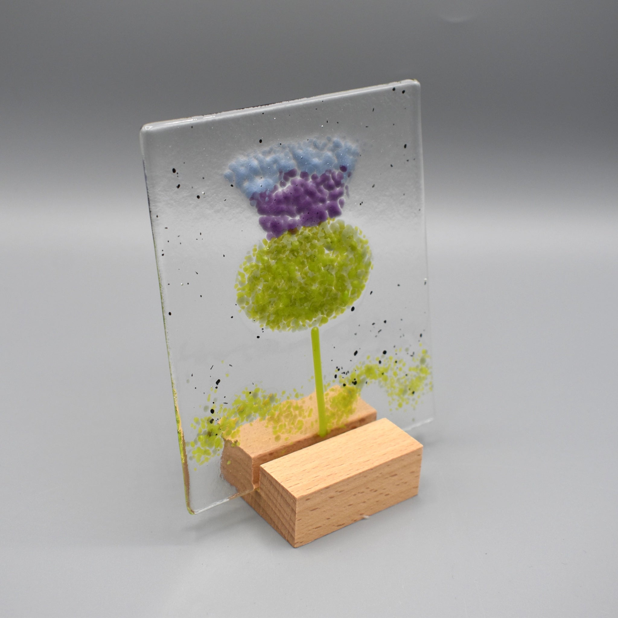 A square glass ornament featuring a thistle and a wooden stand 