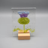 A square glass ornament featuring a thistle and a wooden stand