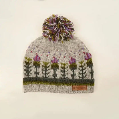 Knitted grey hat featuring a repeating thistle pattern with hearts and a pompom