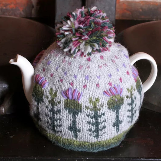 A knitted tea cosy featuring thistles and polka dots and a pompom