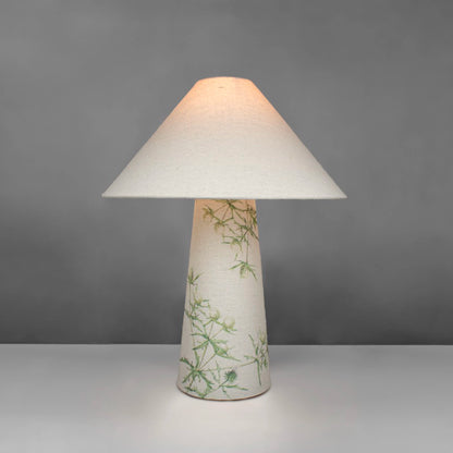 A fabric table lamp with shade and a thistle design on the conical base - lit up