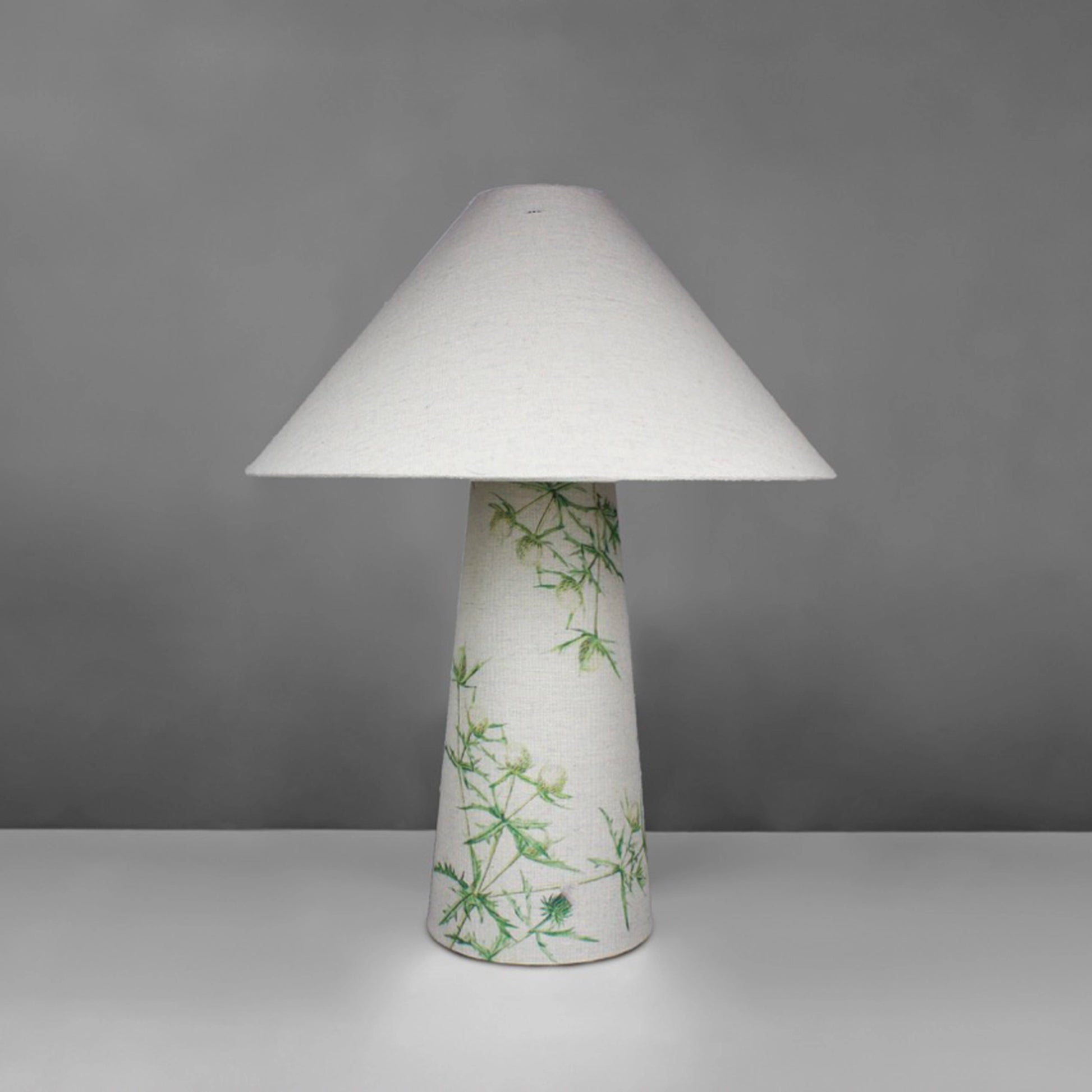 A fabric table lamp with shade and a thistle design on the conical base