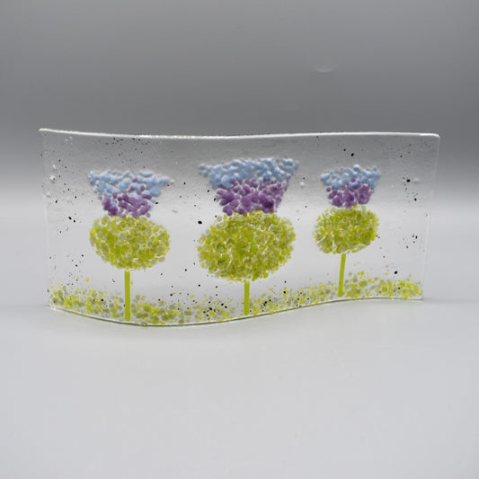 A glass curve sculpture with three thistles in green and purple colours