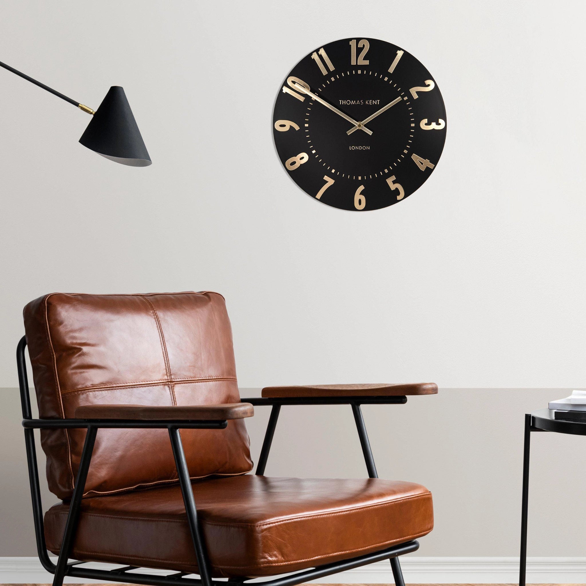 A simple and modern round wall clock in a black colour with gold hands and numbers on wall