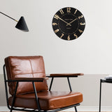 A simple and modern round wall clock in a black colour with gold hands and numbers on wall