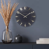 A simple and modern round wall clock in a dark slate grey colour with gold hands and numbers on wall