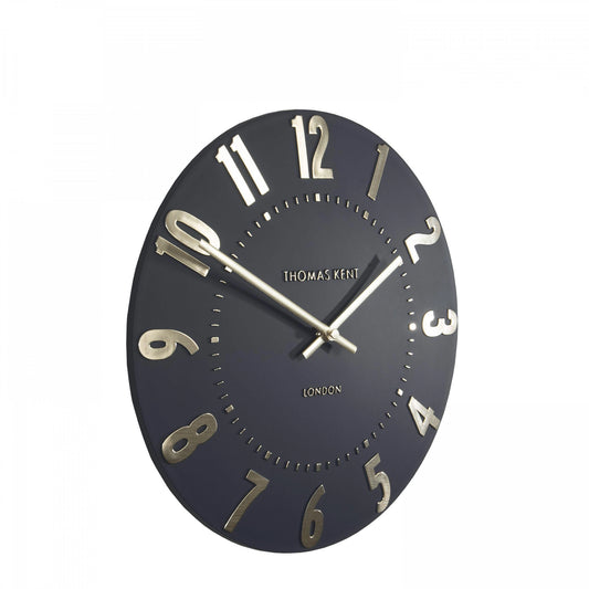 A simple and modern round wall clock in a dark slate grey colour with gold hands and numbers side view