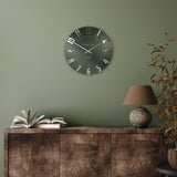 A simple and modern round wall clock in a dark olive green colour with gold hands and numbers on wall