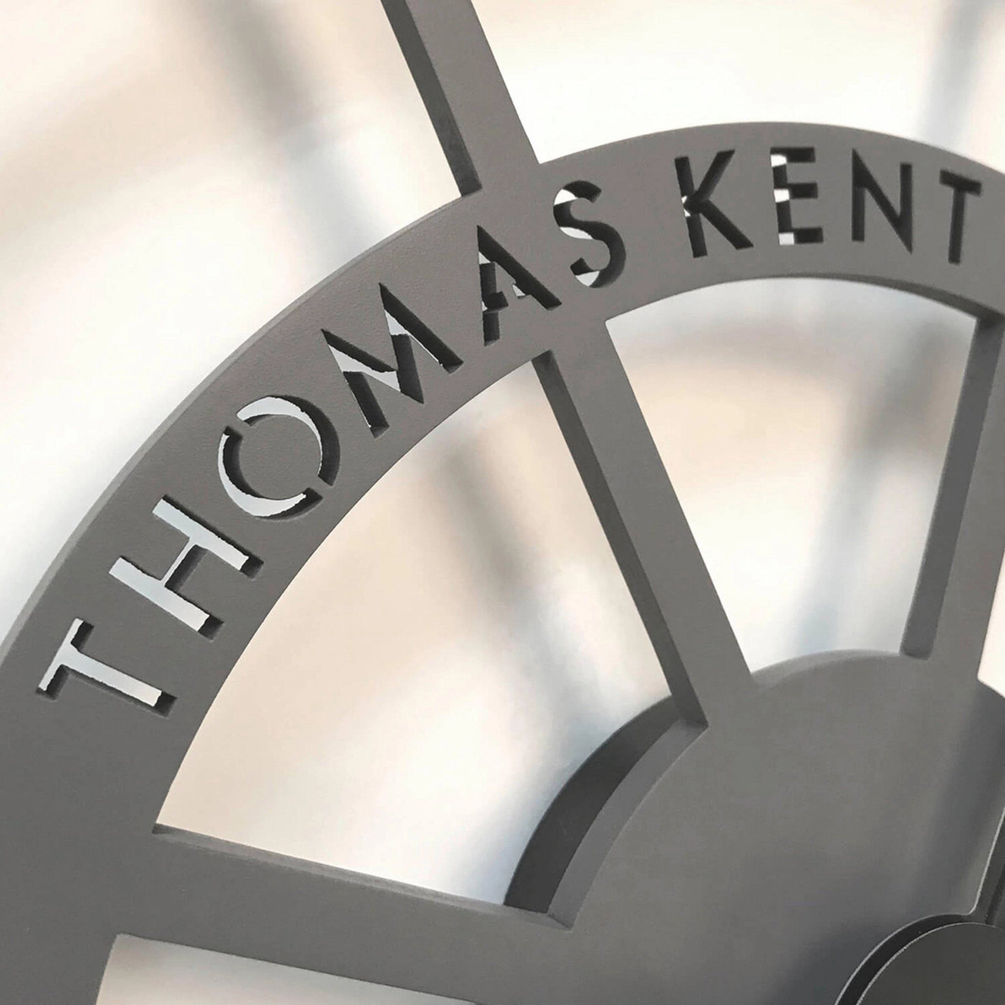 Close-up detail of skeleton wall clock with grey frame and Thomas Kent logo.