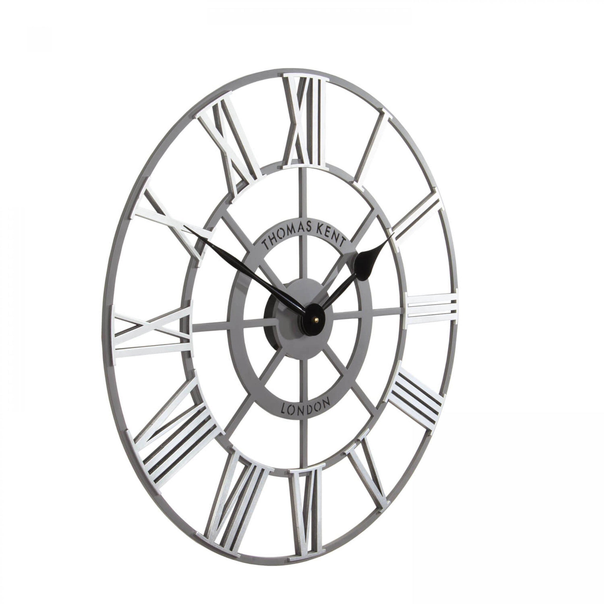 Side view of round skeleton wall clock with grey frame, black hands and silver roman numerals.