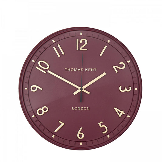 A simple and modern round wall clock in a berry colour with gold hands and numbers